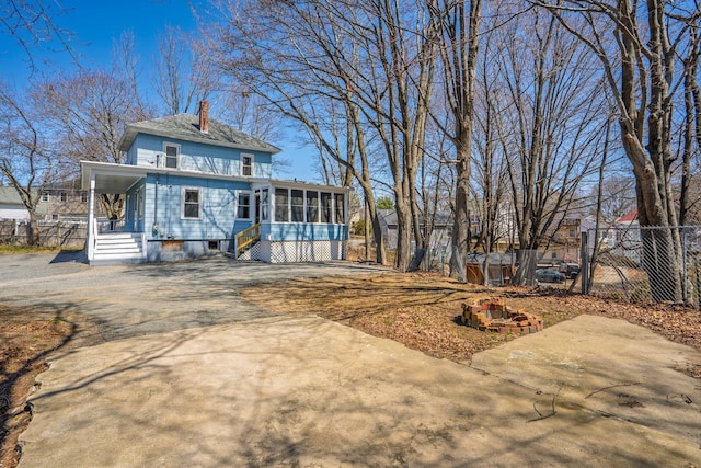 view of front of property featuring a chimney, a sunroom, fence, and driveway