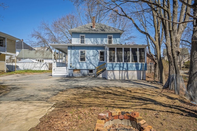 view of front of home with a chimney, a sunroom, fence, and driveway