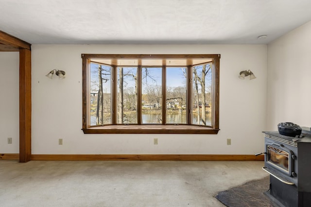 unfurnished living room featuring plenty of natural light, a wood stove, carpet flooring, and baseboards
