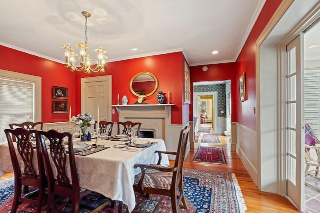 dining space with an inviting chandelier, ornamental molding, a wainscoted wall, and light wood-style flooring