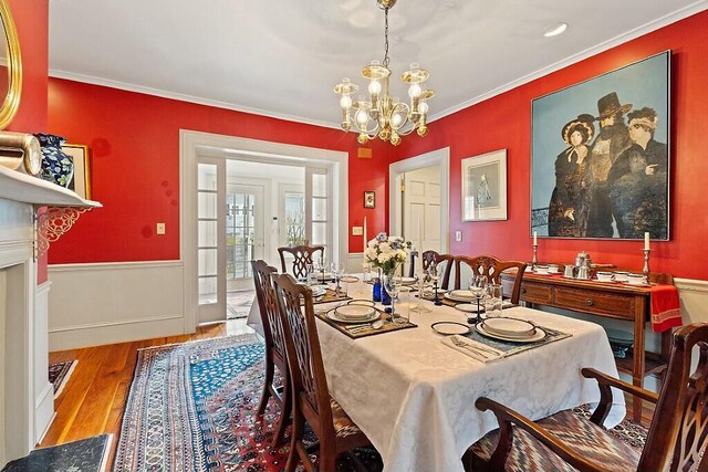 dining area featuring ornamental molding, a wainscoted wall, a chandelier, and wood finished floors