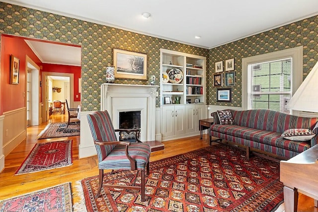 living area featuring wallpapered walls, wood finished floors, a fireplace, and crown molding