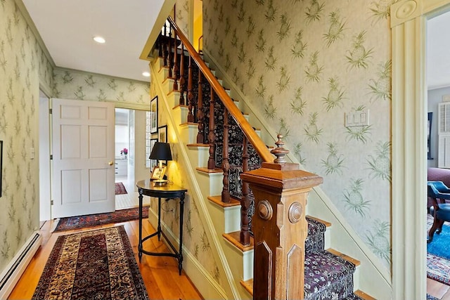 stairs with wallpapered walls, a baseboard heating unit, baseboards, recessed lighting, and wood finished floors