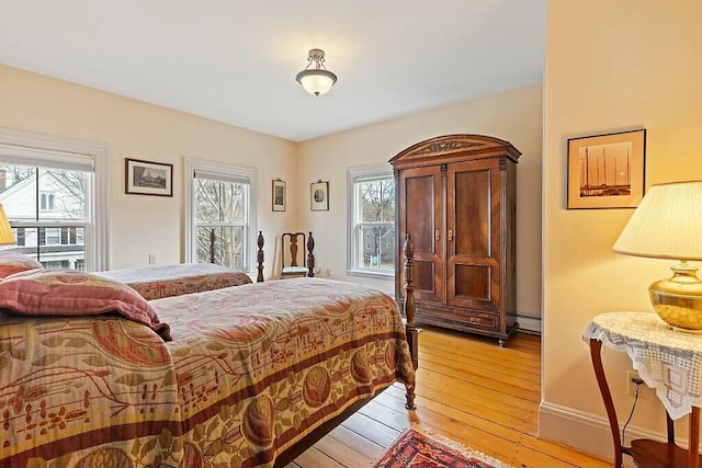 bedroom with a baseboard heating unit, multiple windows, and light wood finished floors