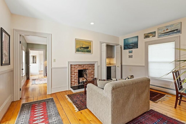living room featuring light wood-type flooring, baseboard heating, and a brick fireplace
