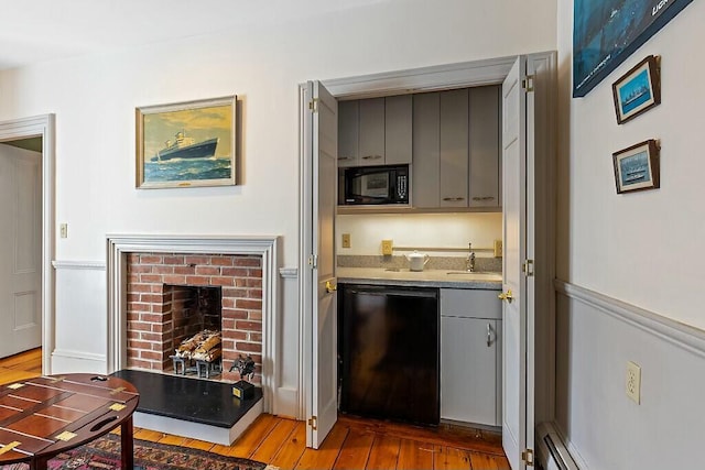 bar featuring hardwood / wood-style floors, black appliances, a brick fireplace, a sink, and wet bar