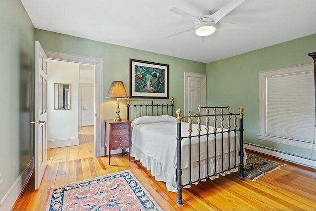 bedroom featuring baseboards, light wood-type flooring, ceiling fan, and a baseboard radiator