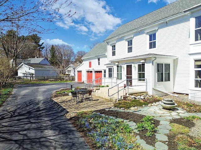 exterior space featuring fence, aphalt driveway, a shingled roof, a garage, and a patio area