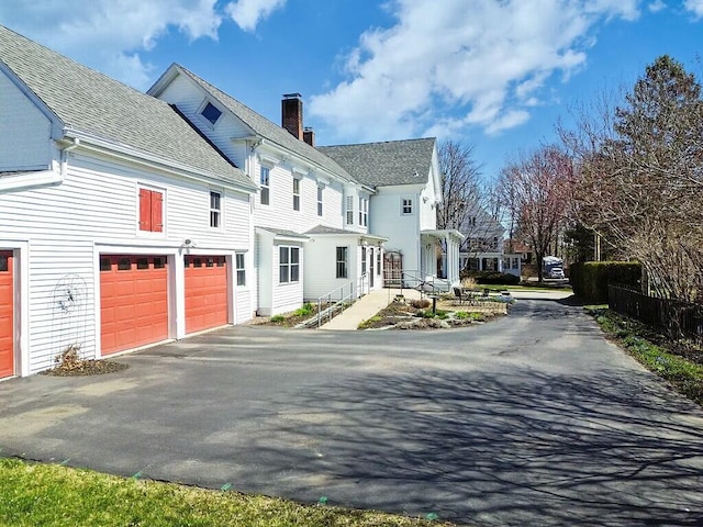 view of home's exterior with a chimney, aphalt driveway, a shingled roof, and an attached garage