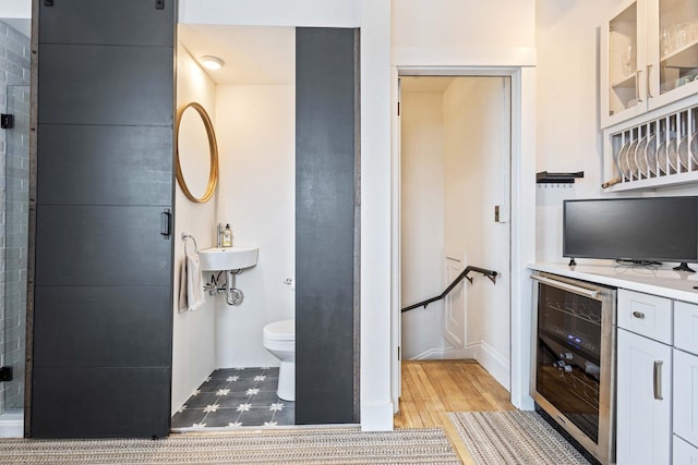 full bath with wood finished floors, toilet, beverage cooler, baseboards, and a sink