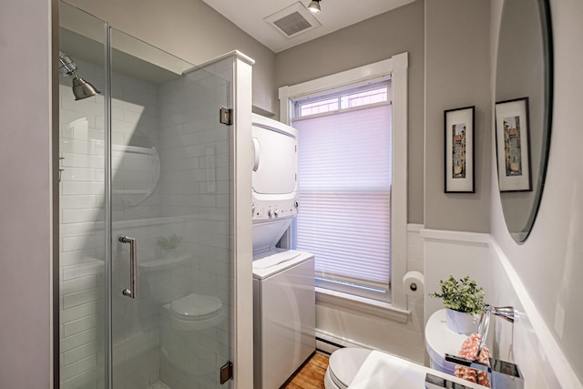 bathroom featuring visible vents, stacked washer and dryer, wood finished floors, toilet, and a shower stall
