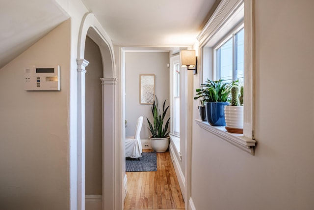 hall featuring baseboards, arched walkways, light wood-style flooring, and ornate columns