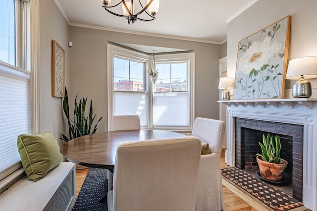 dining room with an inviting chandelier, ornamental molding, light wood-style flooring, and a brick fireplace