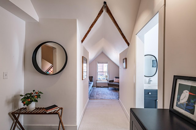 hallway featuring light colored carpet, lofted ceiling, and baseboards