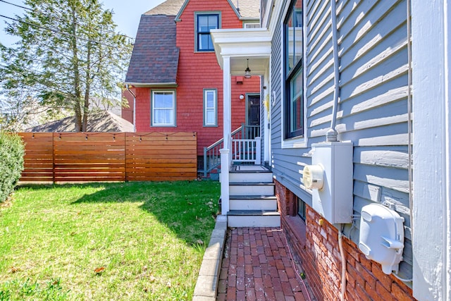 view of exterior entry featuring a lawn, fence, and a shingled roof