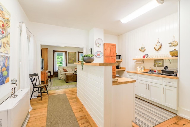 kitchen featuring white cabinets, a sink, light wood-style floors, open shelves, and wood counters