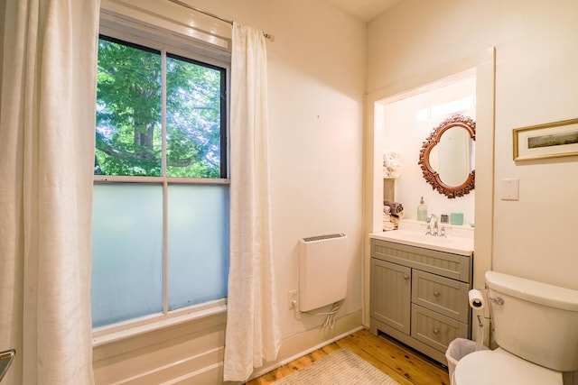 bathroom with vanity, toilet, heating unit, and wood finished floors