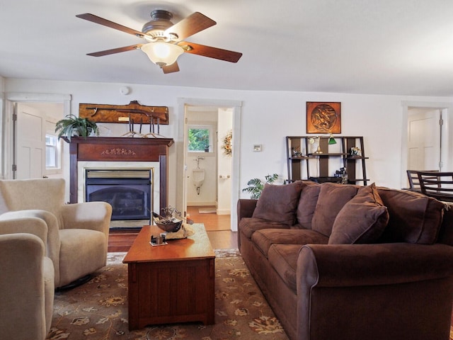 living area with wood finished floors, ceiling fan, and a glass covered fireplace