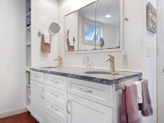 full bathroom featuring double vanity, a sink, wood finished floors, and baseboards