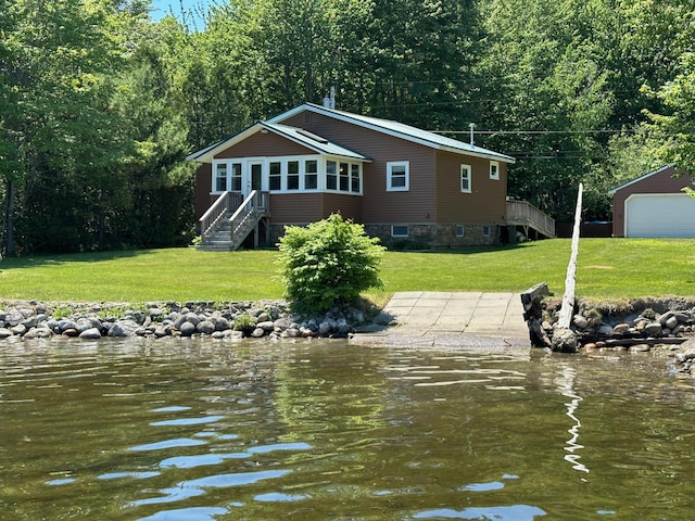 rear view of house with a detached garage, a water view, and a lawn