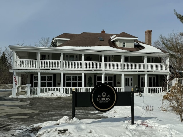 snow covered property featuring a chimney and a balcony