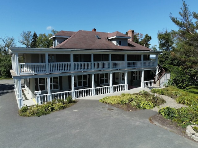 exterior space with stairway, a porch, a chimney, and a balcony