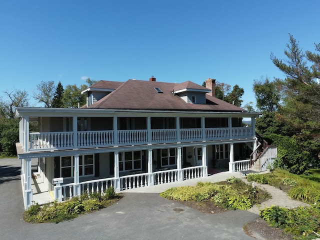 exterior space with stairway, a porch, a chimney, and a balcony