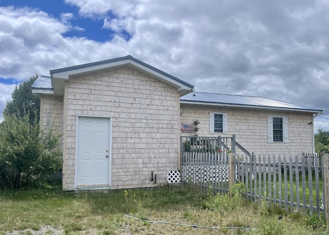 rear view of house featuring an outdoor structure, fence, and metal roof
