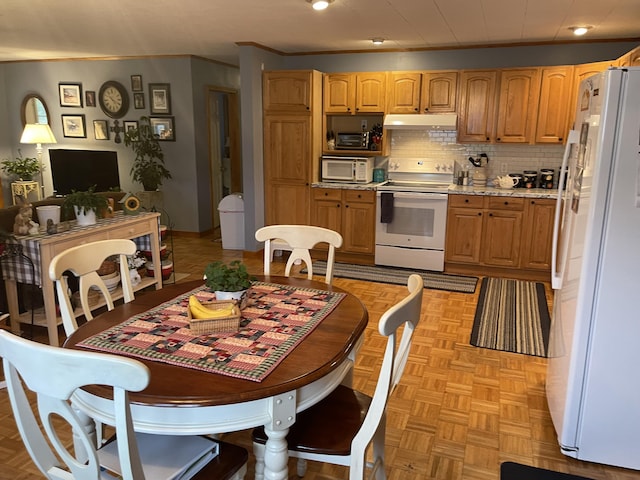 kitchen featuring light stone counters, under cabinet range hood, white appliances, crown molding, and decorative backsplash