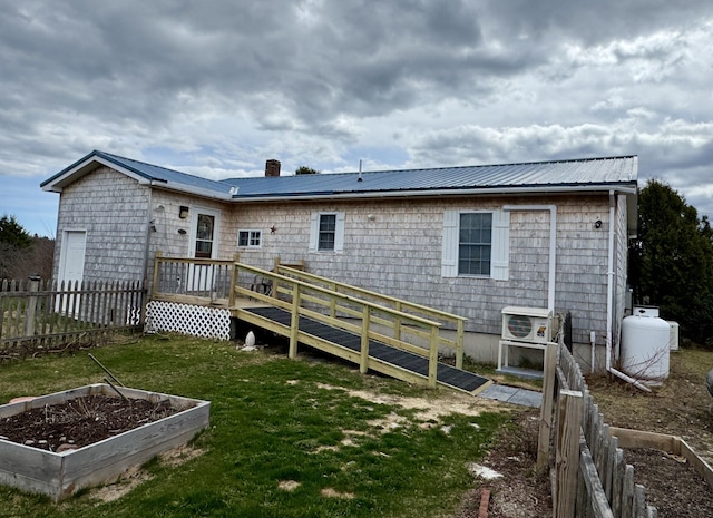 rear view of house with fence, a lawn, a garden, and metal roof