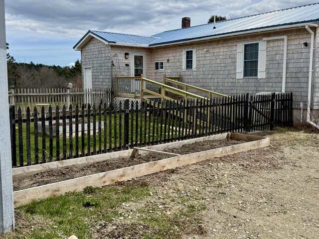 rear view of property featuring metal roof, a garden, a chimney, and fence