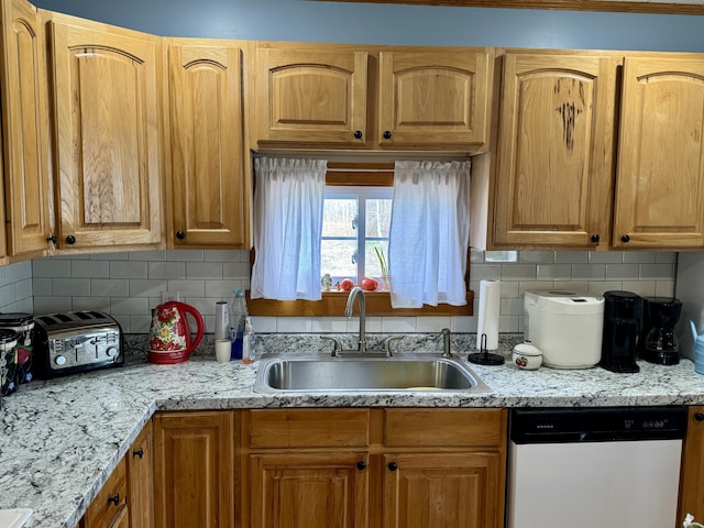 kitchen with dishwasher, light stone countertops, decorative backsplash, and a sink