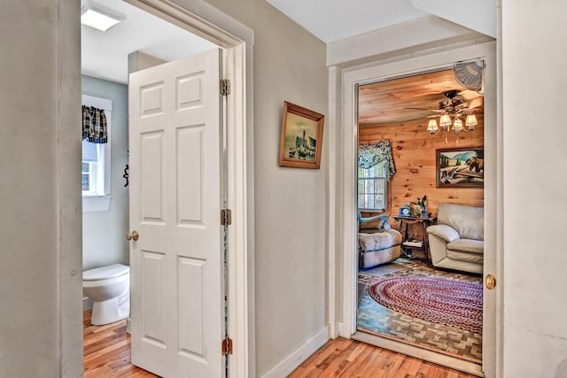 hallway featuring baseboards, light wood finished floors, and wooden walls