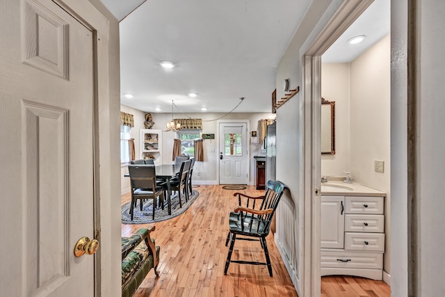 corridor with a sink, baseboards, a notable chandelier, recessed lighting, and light wood-style flooring