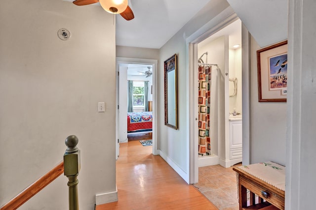hall featuring light wood-style floors, baseboards, and an upstairs landing