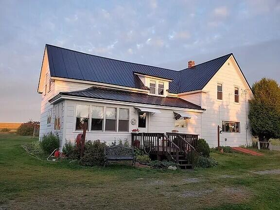 rear view of house featuring a lawn, a chimney, a wooden deck, and metal roof
