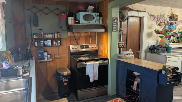 kitchen with blue cabinets, stainless steel electric stove, wall chimney exhaust hood, a sink, and wooden walls