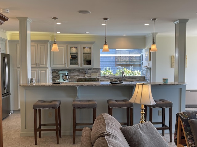 bar featuring decorative backsplash, light tile patterned floors, decorative columns, ornamental molding, and freestanding refrigerator
