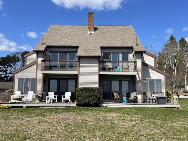 back of house featuring a lawn, a shingled roof, a chimney, and a balcony