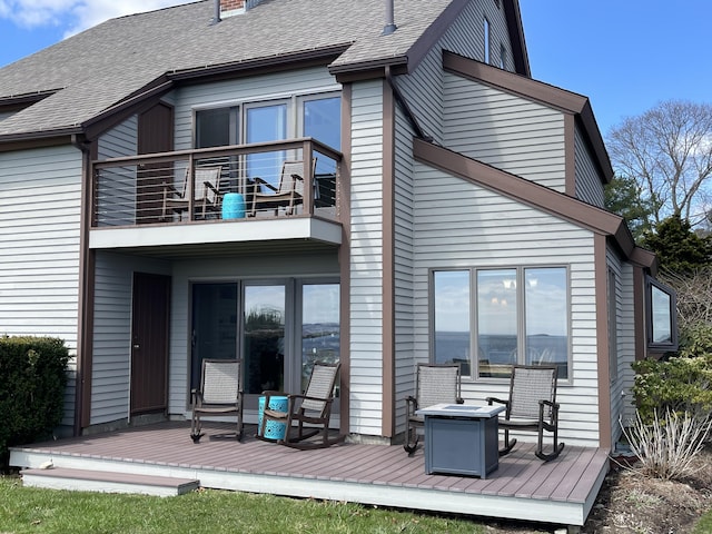 back of property featuring a chimney, roof with shingles, a deck, and a balcony