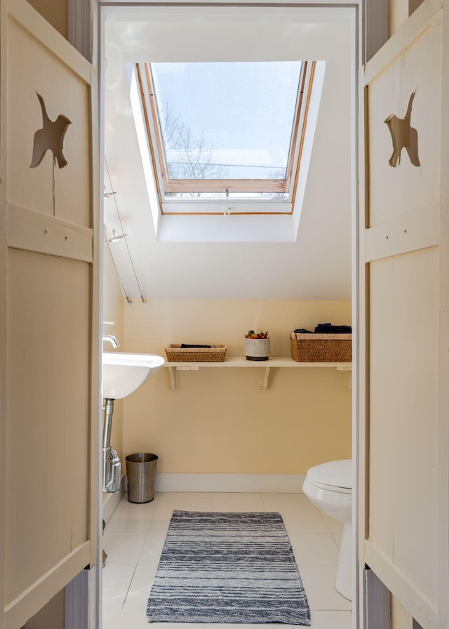 bathroom featuring toilet, a skylight, baseboards, and tile patterned flooring
