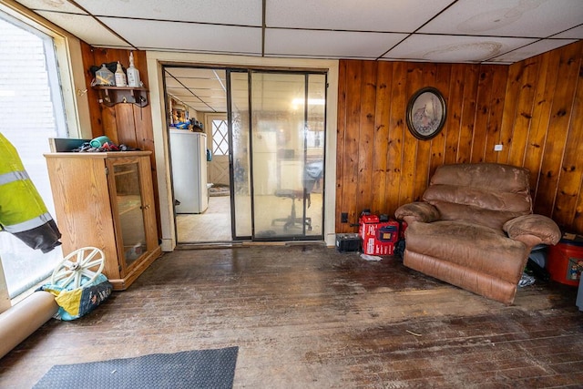 living room with wood walls, a drop ceiling, and hardwood / wood-style flooring
