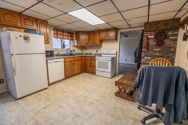kitchen with brown cabinetry, a sink, a drop ceiling, and white appliances