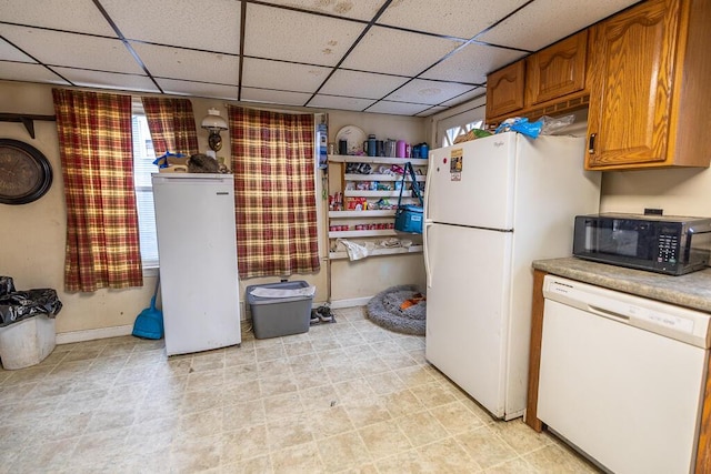 kitchen with brown cabinets, baseboards, a drop ceiling, and white appliances