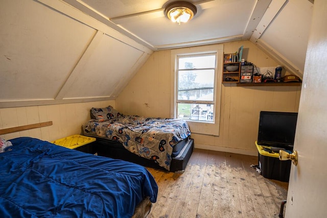 bedroom featuring wood walls, hardwood / wood-style floors, and lofted ceiling
