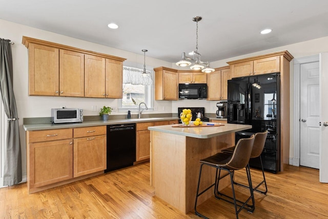 134 Yale St, Portland, ME 04103 - kitchen featuring black appliances, a sink, a kitchen island, a breakfast bar, and light wood-style floors