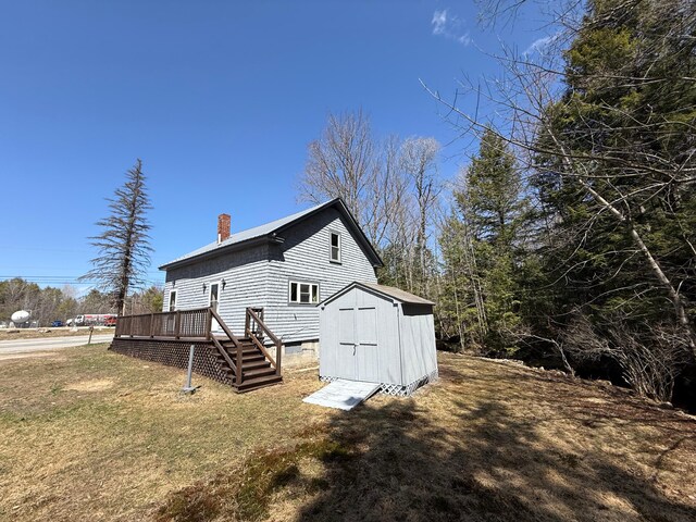 633 Norway Rd, Harrison, ME 04040 - view of side of property with an outdoor structure, a storage unit, a wooden deck, a chimney, and a lawn