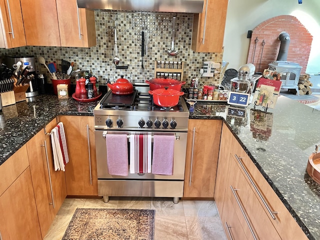 16 Howard Ave Unit 16, Wells, ME 04090 - kitchen with wall chimney range hood, decorative backsplash, a wood stove, stainless steel stove, and dark stone counters