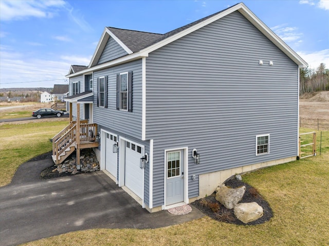 view of home's exterior with a yard, an attached garage, a shingled roof, and aphalt driveway