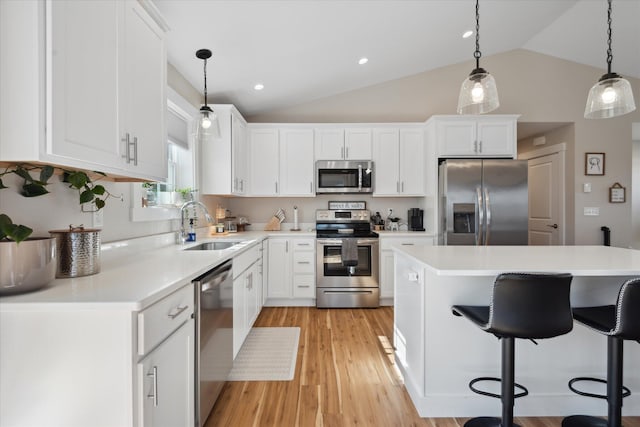 kitchen featuring a breakfast bar, a sink, light wood finished floors, appliances with stainless steel finishes, and vaulted ceiling